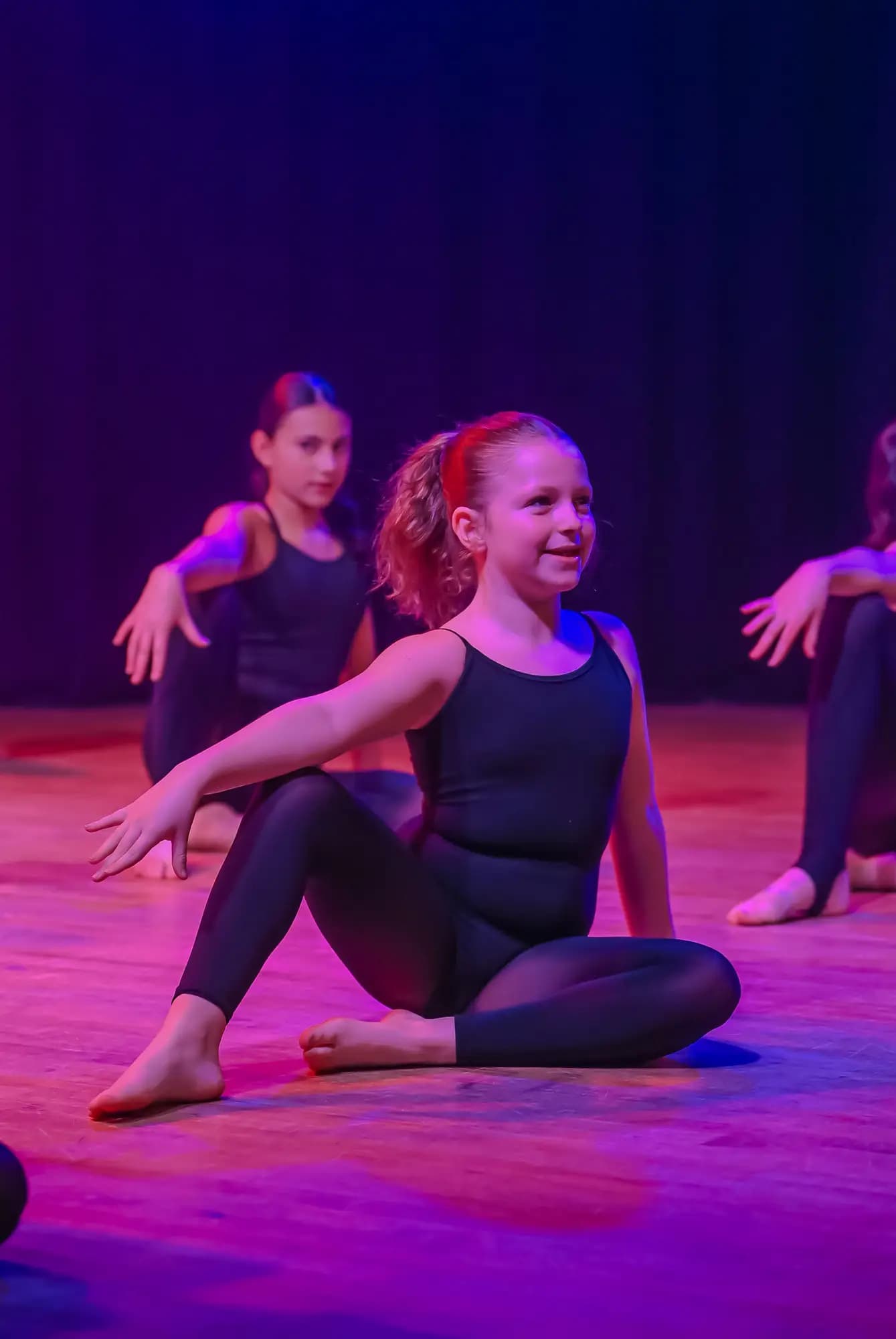Young dancer seated in a stage pose under purple light